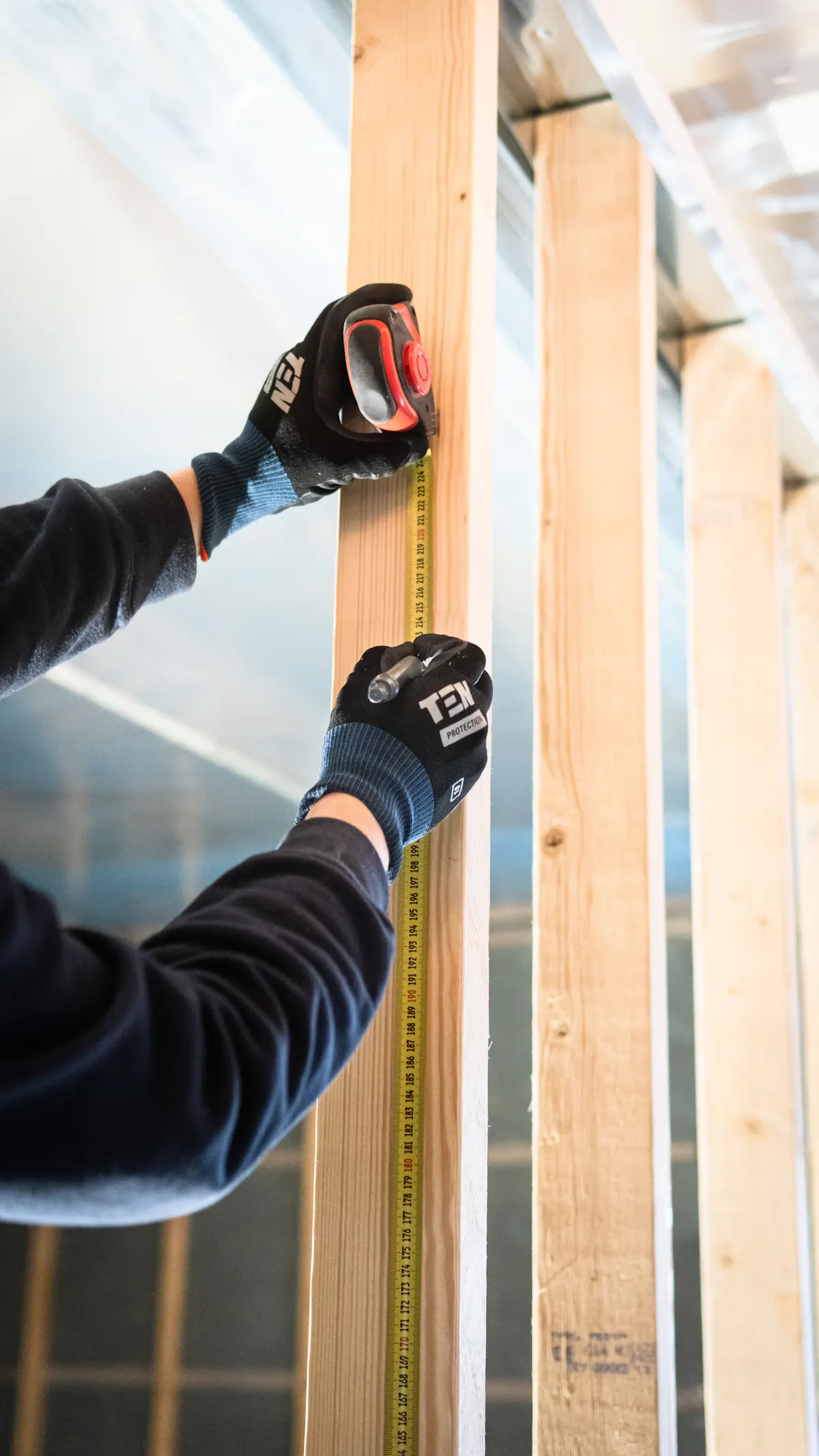 Person measuring timber wall framing with a tape measure